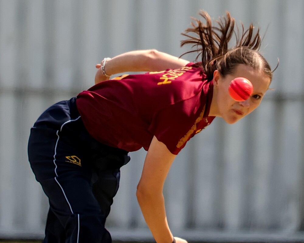 A bowler with their face partly covered by a cricket ball.